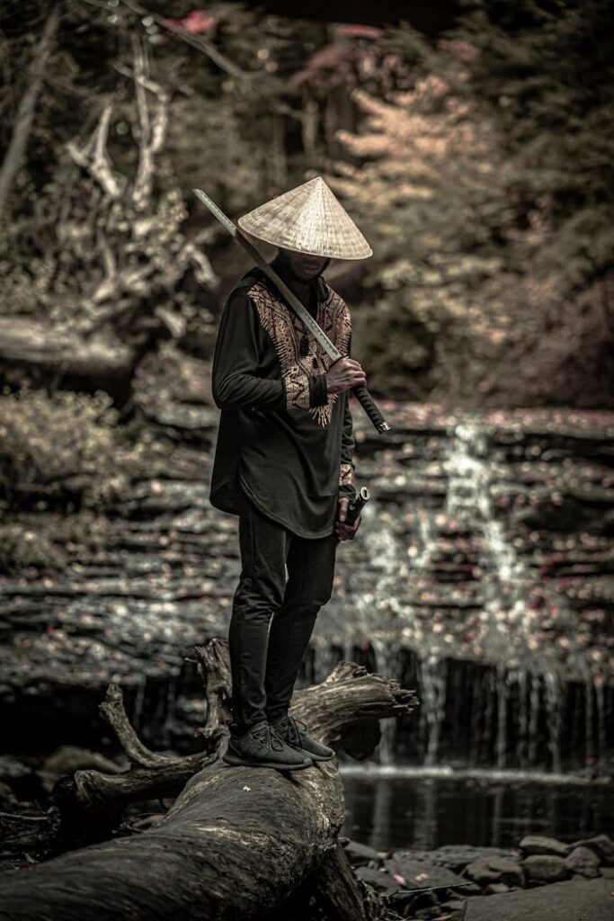 pexels-photo-5971327 A man in traditional samurai attire stands by a waterfall, holding a sword.